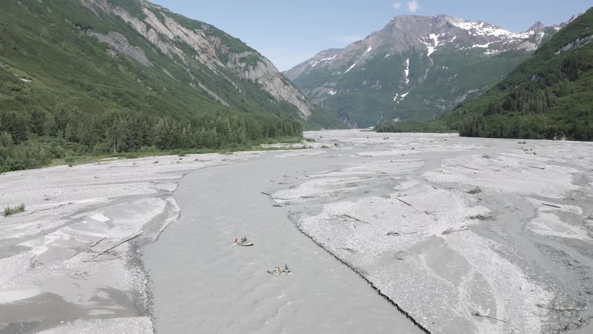 People are traveling in kayaks through the stream by the mountains