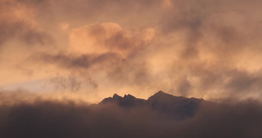 The clouds in the sky sit on the peak of the mountain