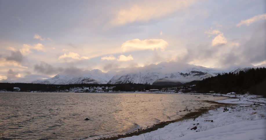 A lake with ripples caused by the wind its banks covered in snow and a snowcovered mountain visible in the distance at midday