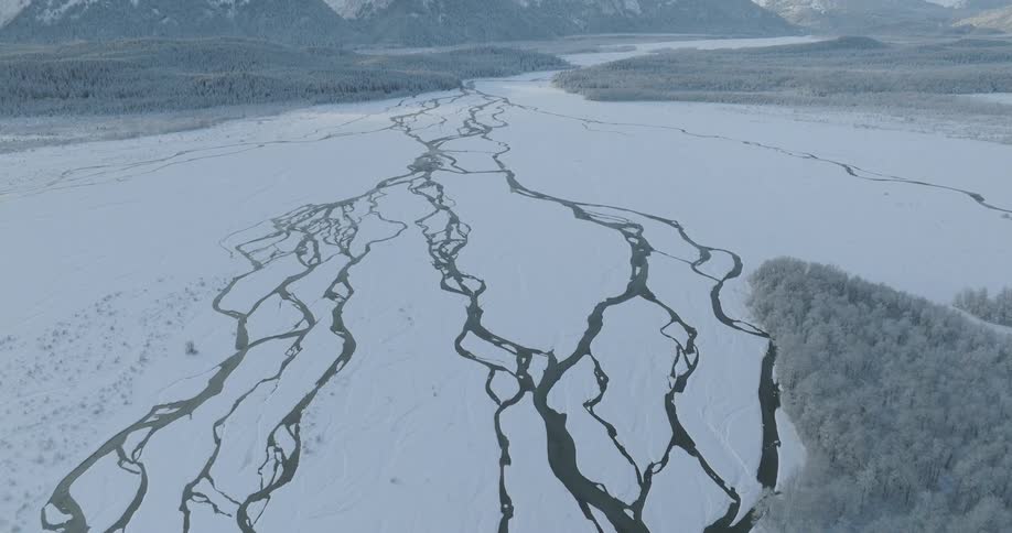 A frozen river with forests on the side and large snowcovered mountains in the horizon