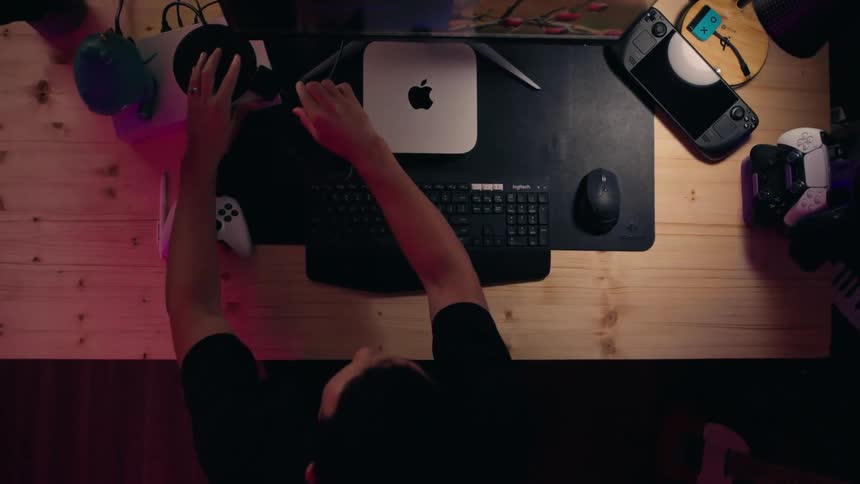 Young man connects a component while sitting in front of a table holding a computer and gaming equipment