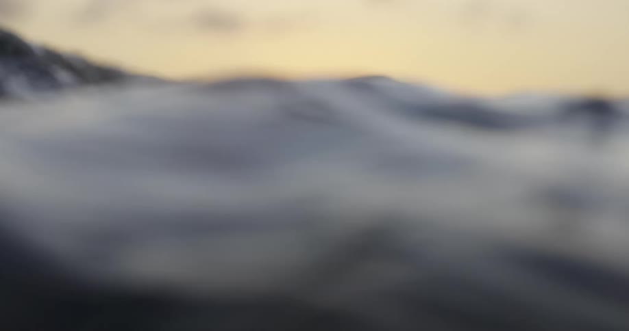 A closeup view of ocean waves with the sun setting in the background casting a warm glow over the water
