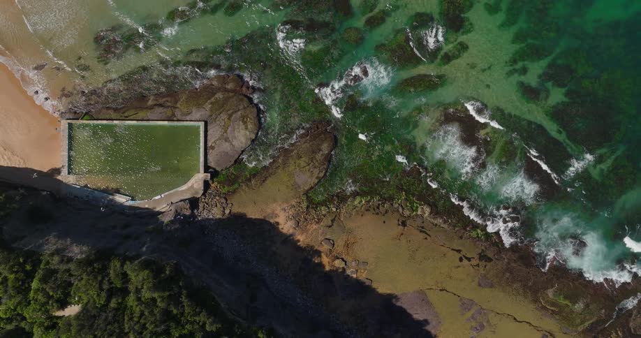 Waves crash onto the beach at midday with a natural rock pool situated just beside the shoreline