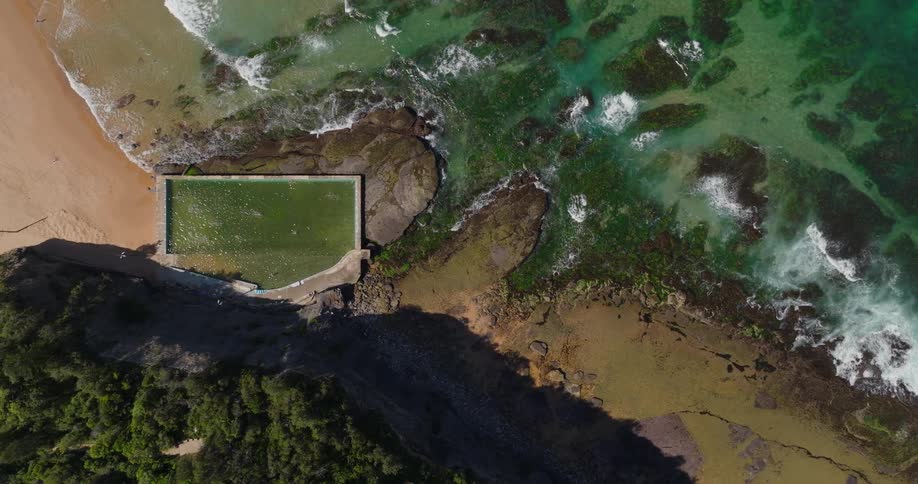 Aerial view of a coastal ocean pool surrounded by rocks and waves along a beach shoreline