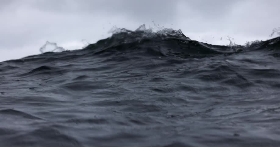 A large ocean wave rises under an overcast sky shot from a low angle to highlight its power
