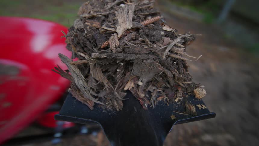 Point of view of a shovel collecting dirt and dry leaves being placed inside a red construction material cart