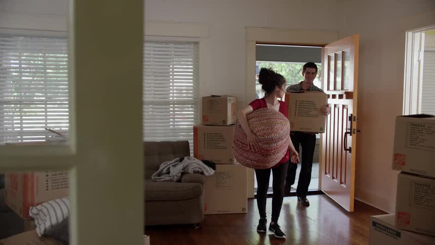 A family enters a house carrying boxes
