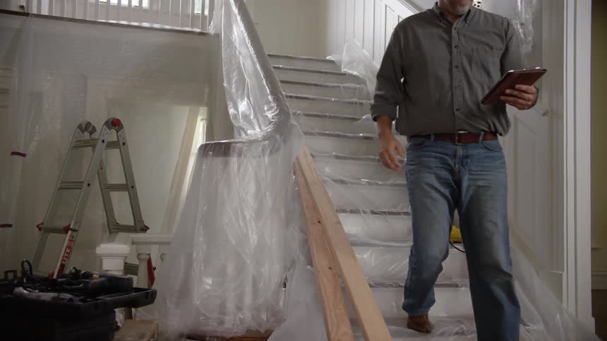 Man holding a clipboard gets up off stairs in a house being renovated