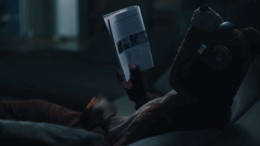 Man sitting on the couch eating a slice of bread and reading a magazine