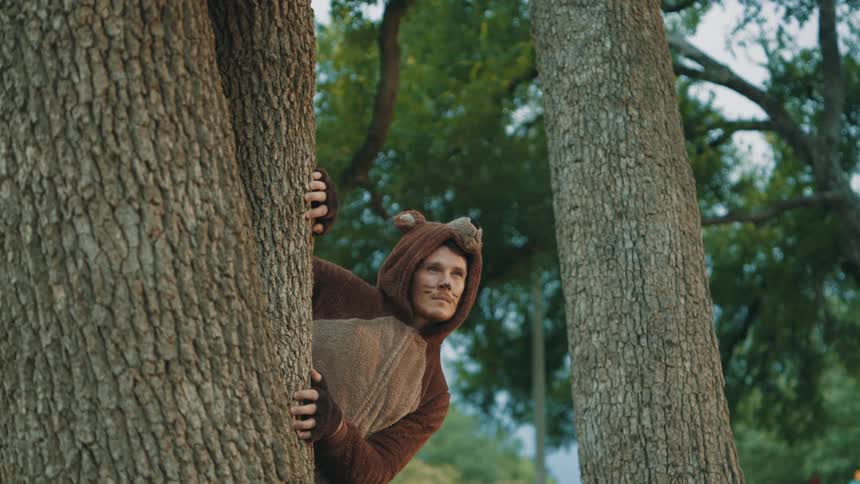 A man wearing a bear costume reveals himself from behind a tree