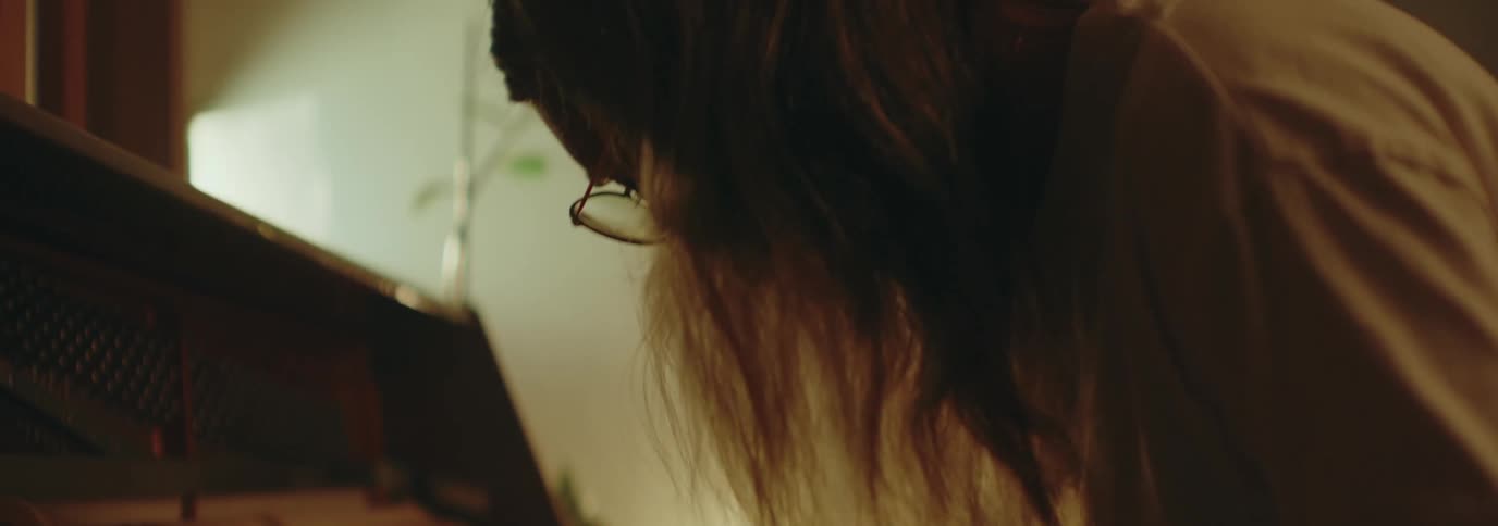A man with long hair and glasses is playing a piano keyboard indoors at midday moving his body to the rhythm