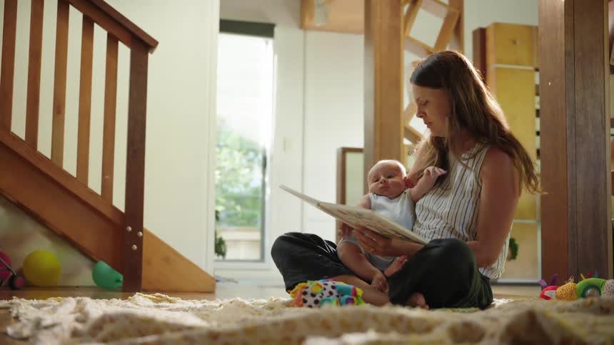 Mother sitting on the carpet and reading a book with a baby on her lap