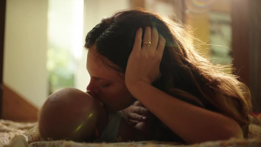 Mother lying down playing and giving her baby a kiss
