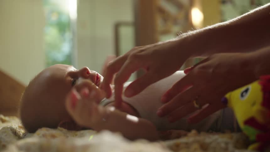 Person tickling the body of a baby lying on a rug