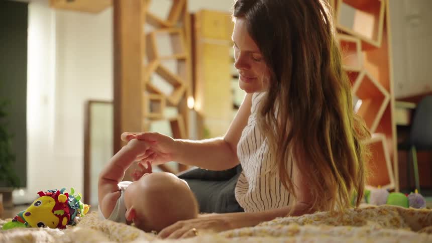 A woman gently interacts with a baby lying on a blanket seemingly engaging in playful activity