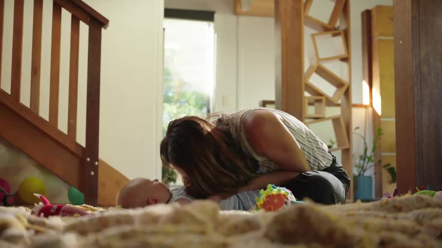 Mother in living room sitting on carpet playing with her baby lying down