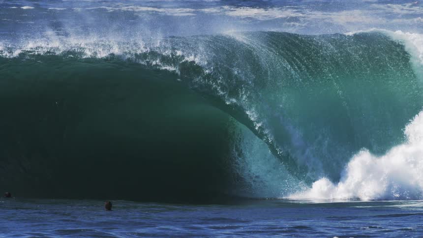 A surfer swims in the ocean as heavy waves crash around him at midday