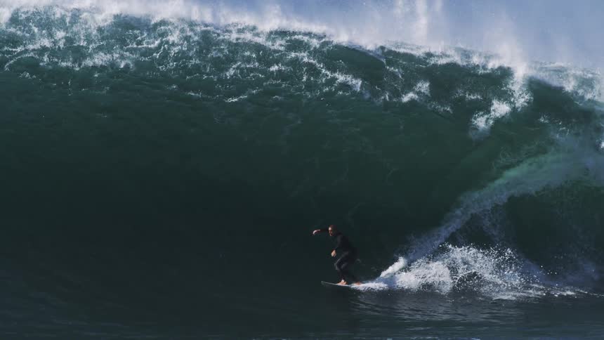 A surfer riding a massive towering wave with spray and foam flying everywhere as they navigate the powerful force of nature
