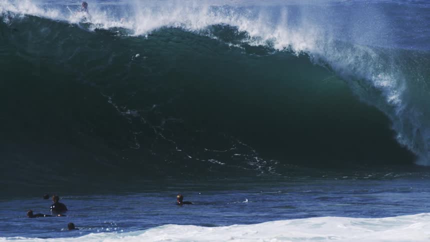 A group of surfers paddling out into the ocean facing a series of large powerful waves