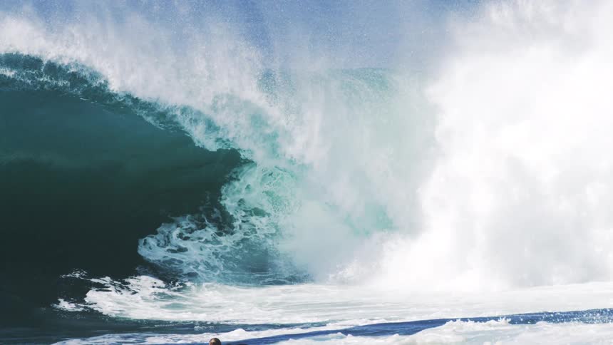 A person swims on a surfboard as heavy waves crash in the ocean at midday