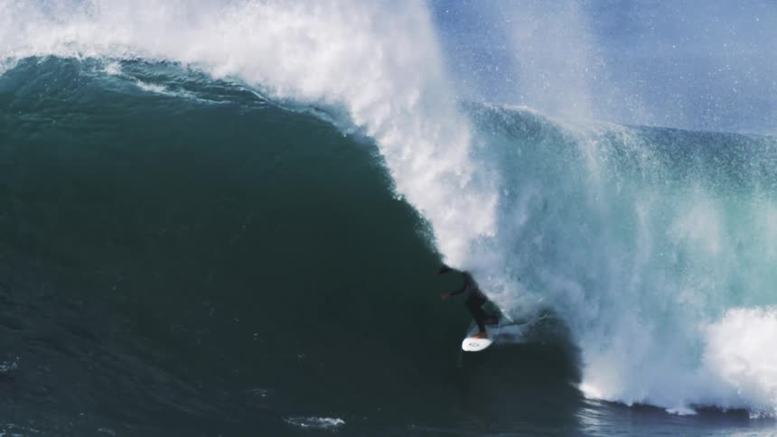 A surfer expertly rides a massive curling wave with spray flying around them