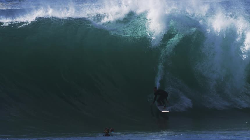 People in the ocean filming a surfer riding a tubular wave