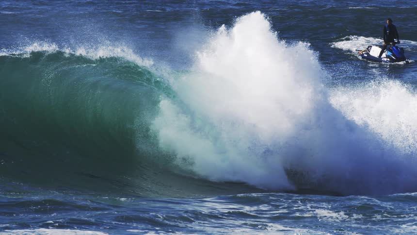 A man is riding a jet ski by a crashing wave