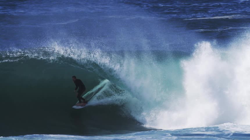 A surfer rides along the face of a large powerful wave with white water cascading down