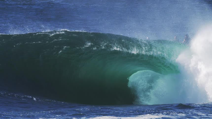 Three surfers preparing to ride a huge wave on a sunny day