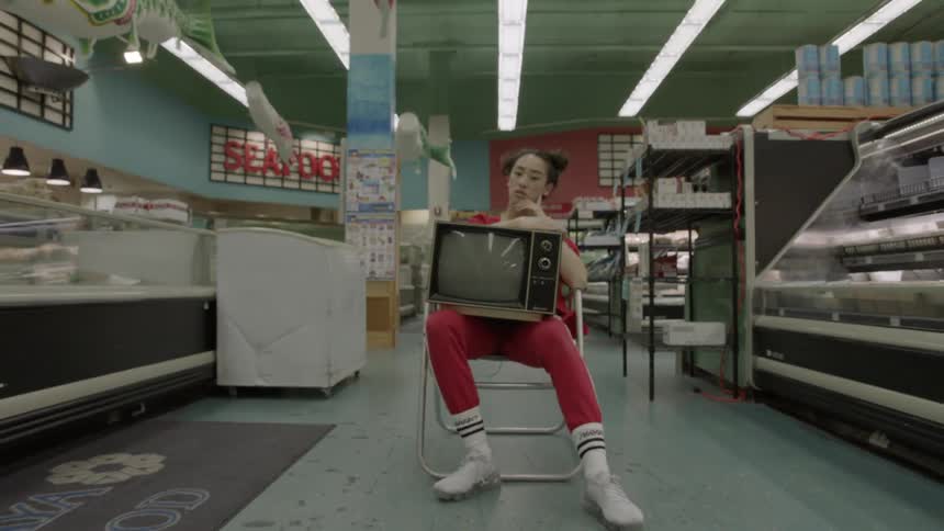 A woman is sitting on a chair holding a tv in a grocery store