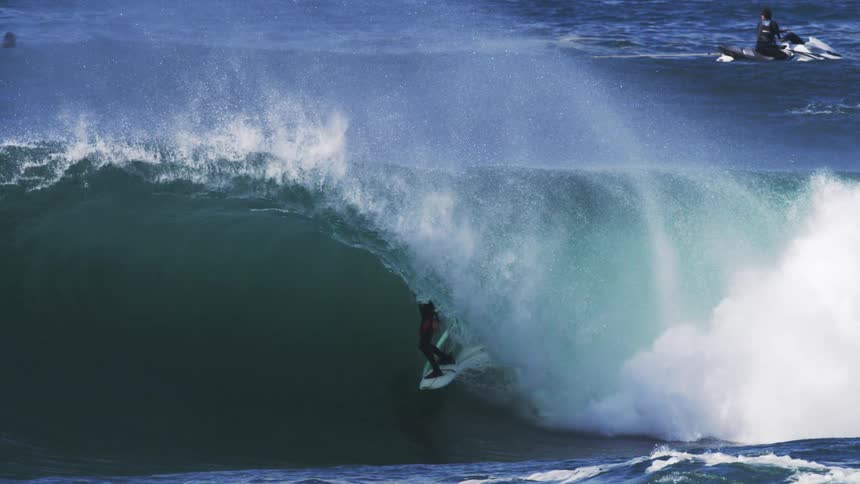 A surfer carves down the face of a massive turquoise wave