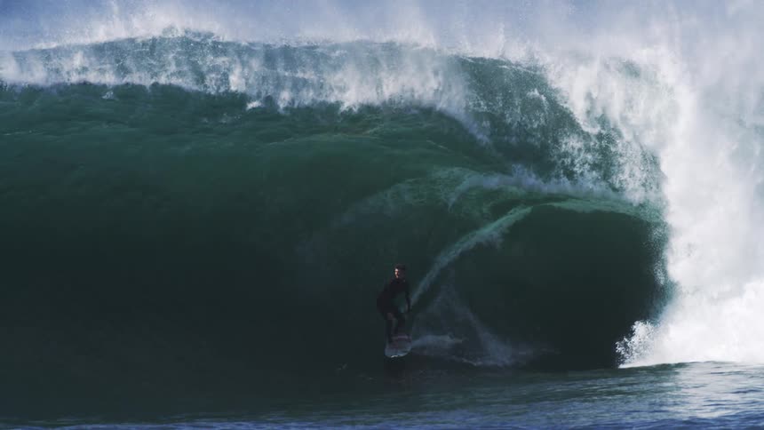 A surfer rides the ocean waves under the bright midday sun