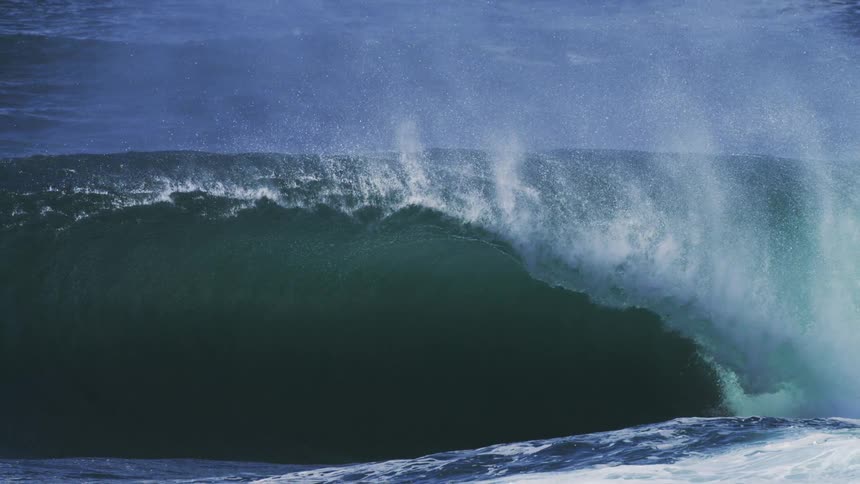 A powerful crashing ocean wave with a cool blue tint appearing to break and spray water into the air