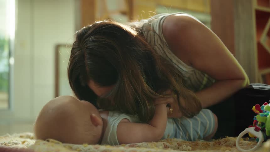 A woman lies on the bed in the bedroom at midday smiling as she kisses her baby on the chest