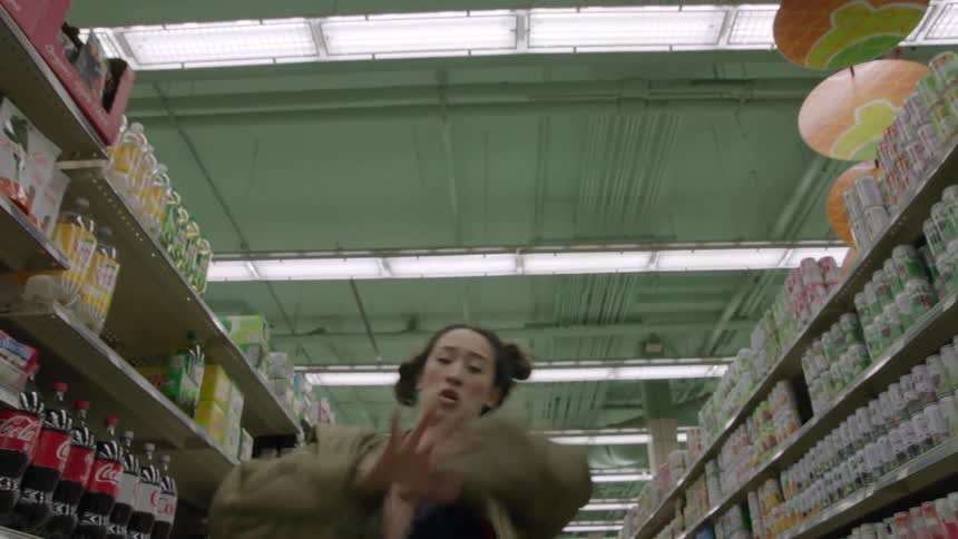 Woman wearing a large green coat doing some funky dance moves in a grocery isle