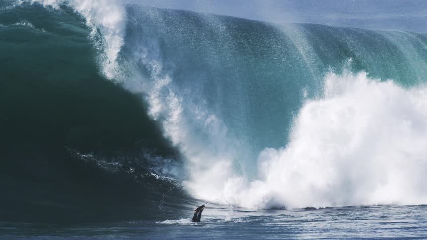 A person dives into the ocean as heavy waves sweep through the water at midday