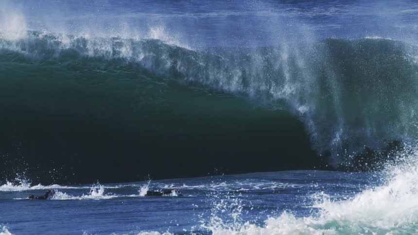 A surfer swims away from a massive ocean wave forming at midday