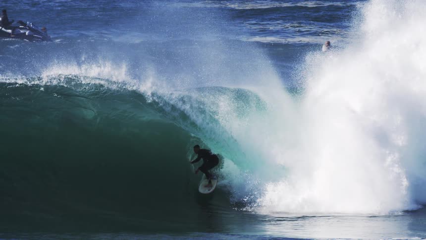 A surfers riding the barrel of a large wave while other people float behind the wave