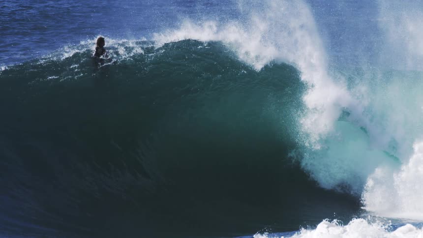 A person rides a gigantic ocean wave in slow motion