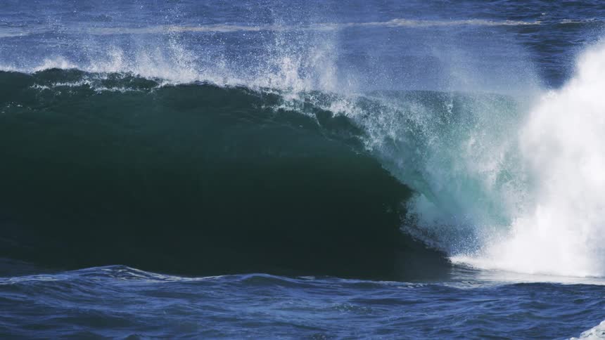 A large ocean wave curls over forming a tunnellike shape with white spray erupting from its crest