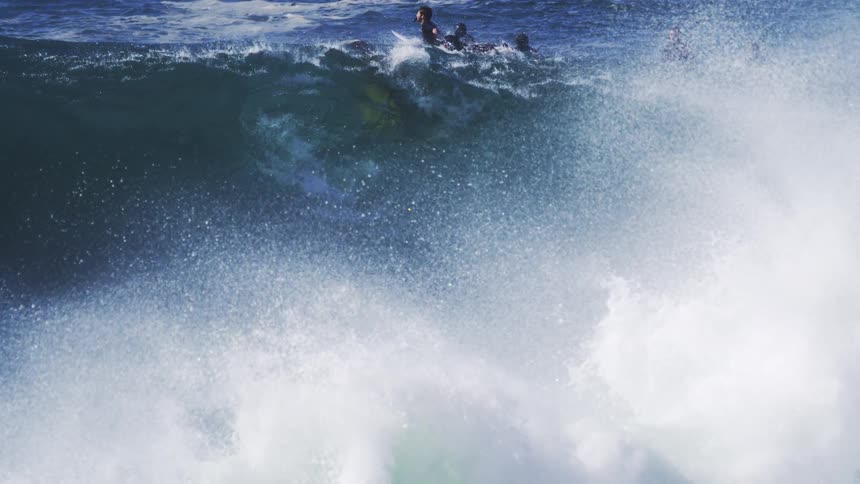 Several people in the ocean lying on their surfboards going over a wave