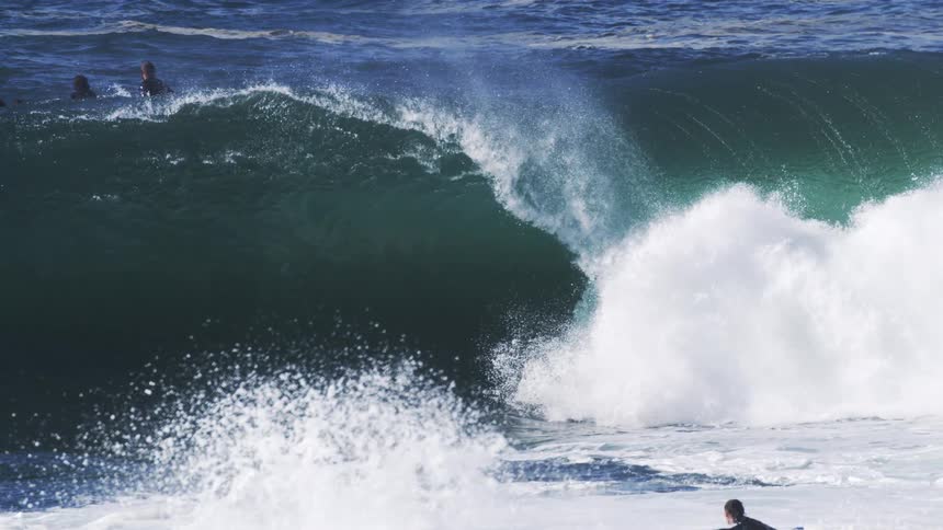 Three people ride a gigantic wave in the open sea in slow motion