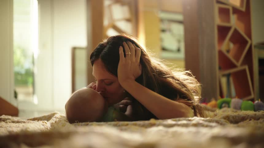 A mother kisses her baby and holds his hand