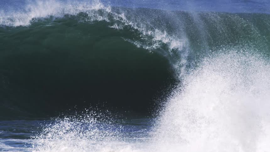 Heavy waves cause the ocean water to rise aggressively splashing and creating foamy surf at midday