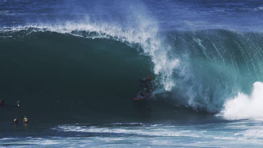 A surfer in a dark suit is engulfed by the hollow of a massive powerful wave