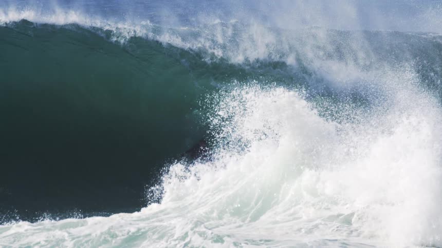 A man surfing a huge wave and higher up on the wave another man coming out of it