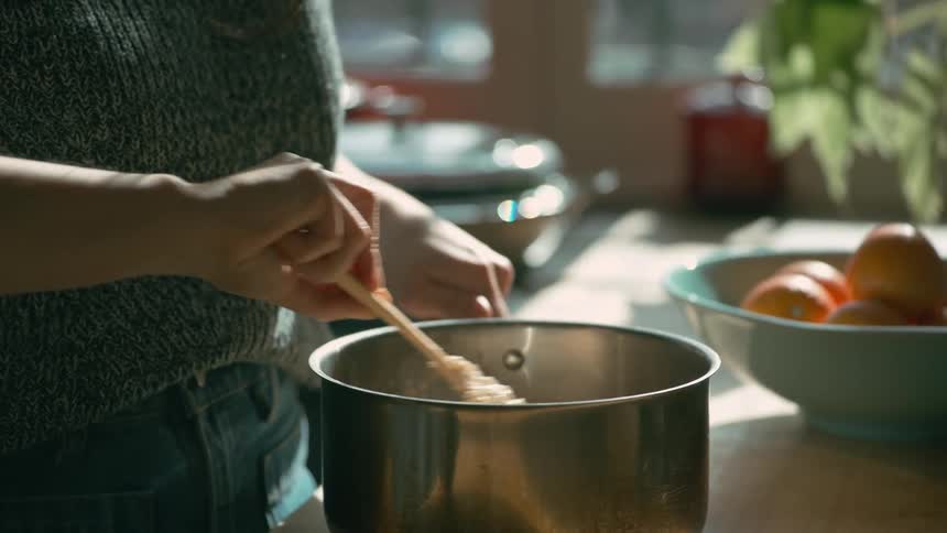A woman stirs a pot of food with a wooden spoon on a kitchen counter