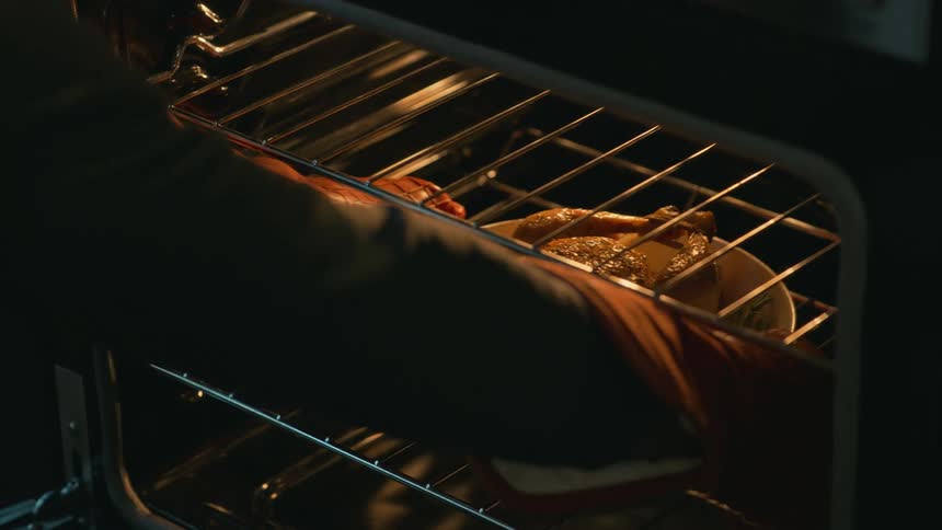 An adult pulls a red pot of roast chicken out of the oven