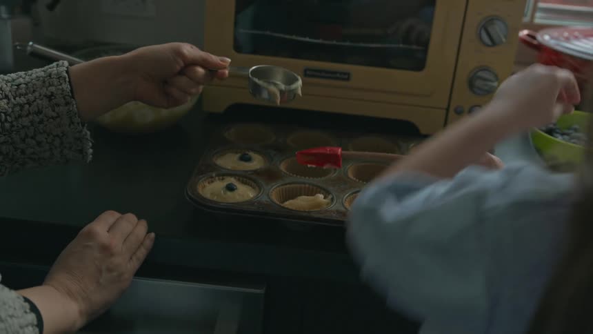 Mother and daughter are placing batter into a muffin baking tray