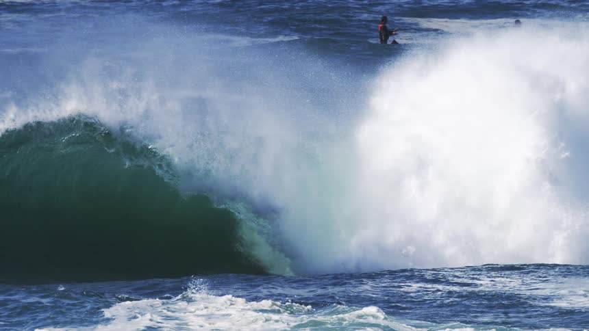 A huge wave crashing while two people are riding jet skis nearby
